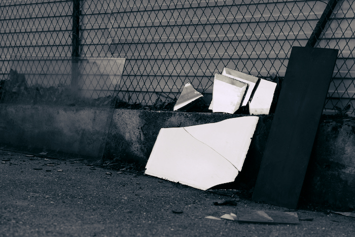 Broken mirror leaning against a fence.